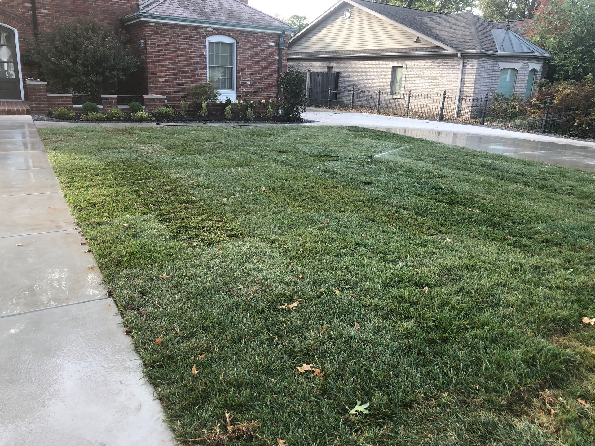 Front yard with a green lawn, concrete driveway, and brick house with a garage.