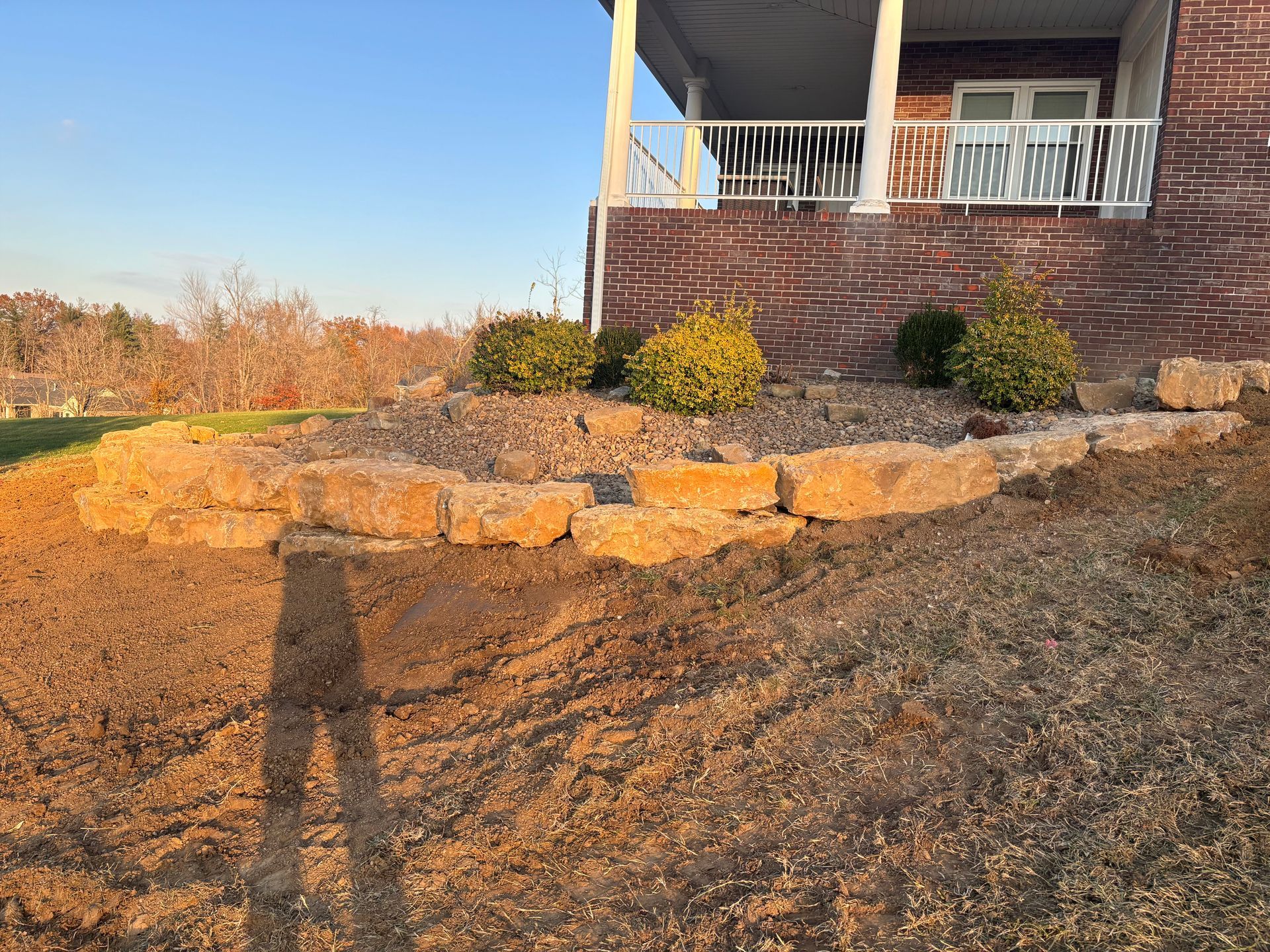 Stone retaining wall and dirt slope beside a brick house porch in warm afternoon light