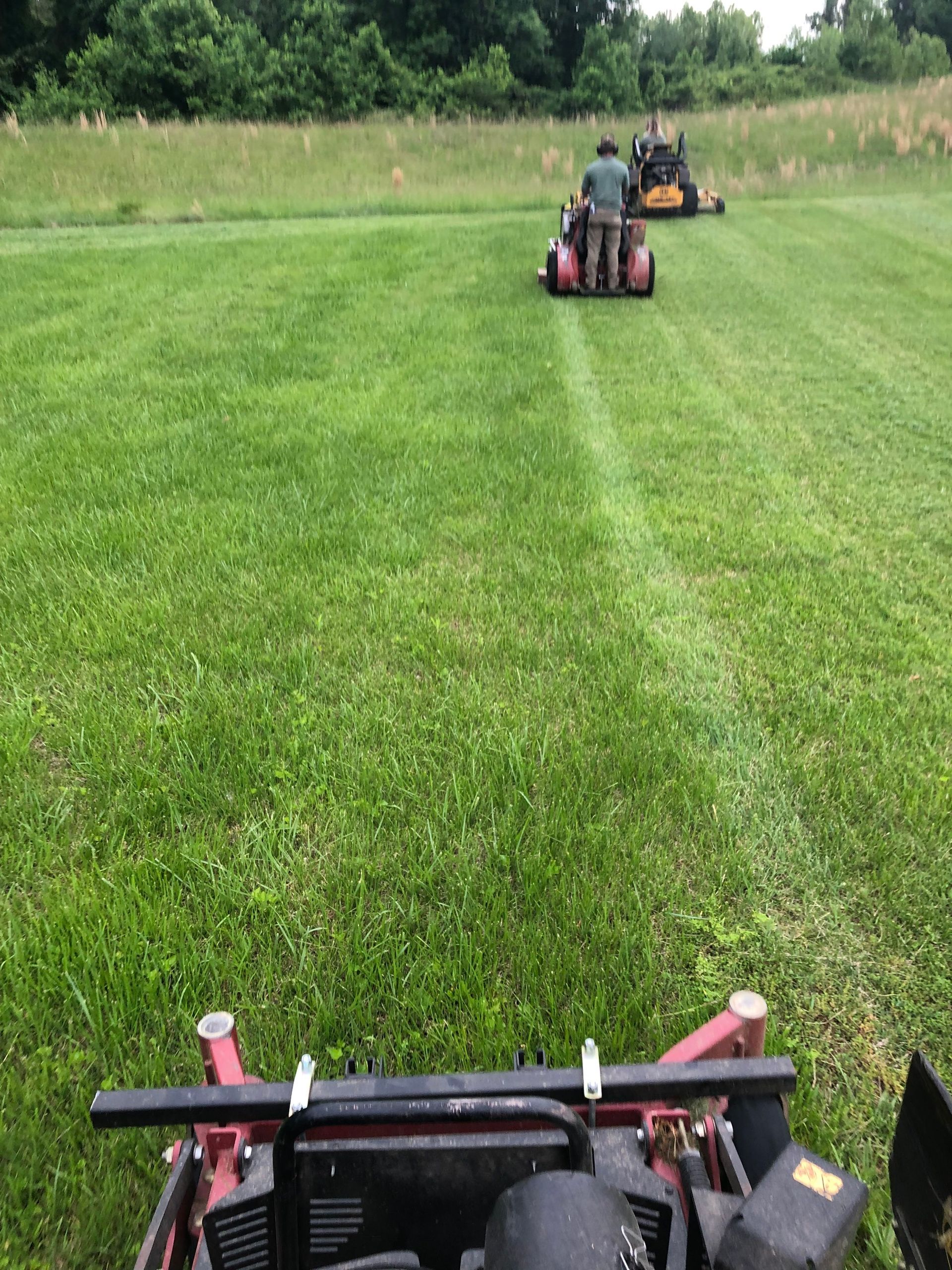 Two mowers cutting a wide green field, seen from one mower in the foreground