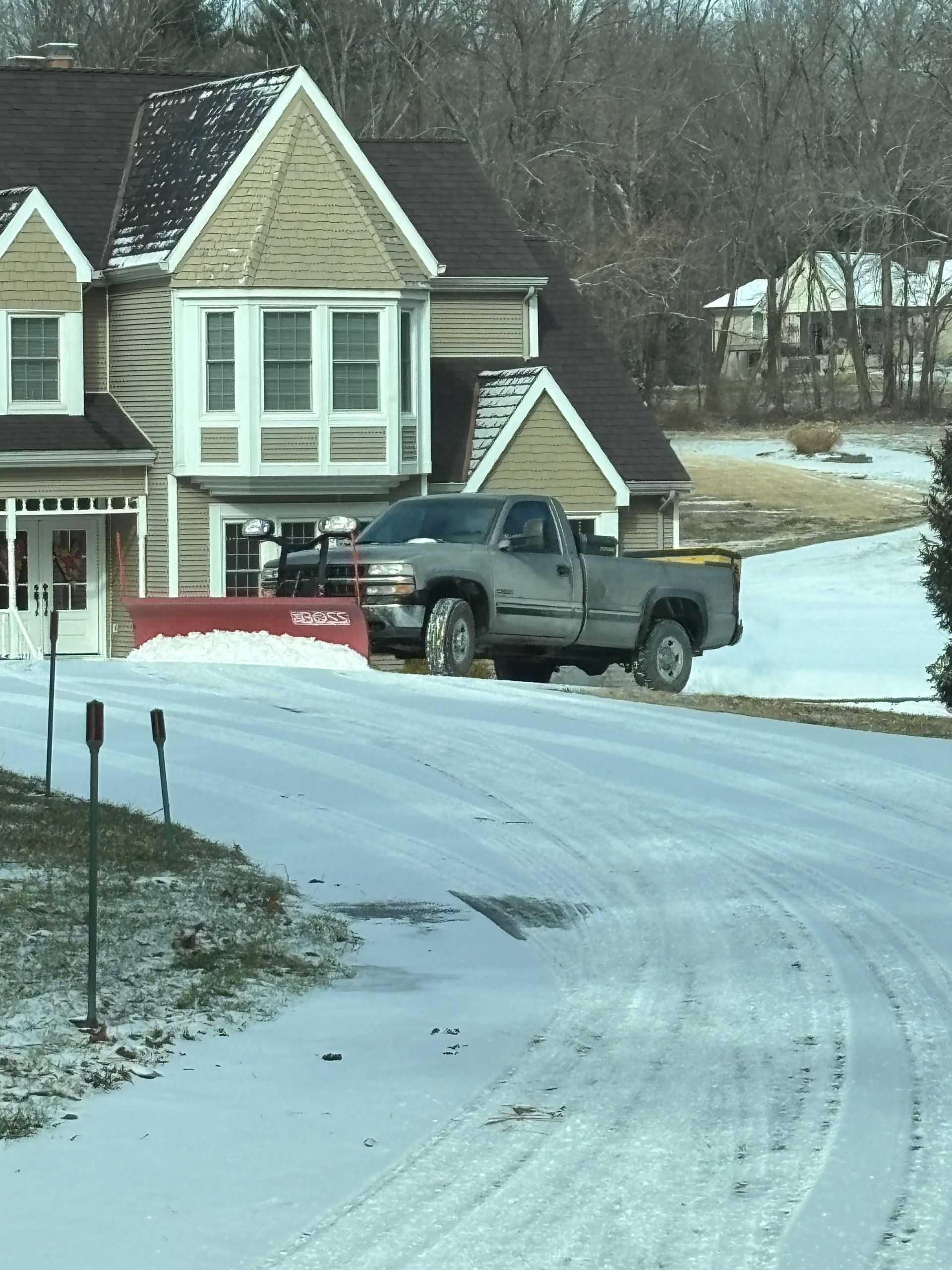Snowy driveway with a gray pickup truck parked beside a suburban house.