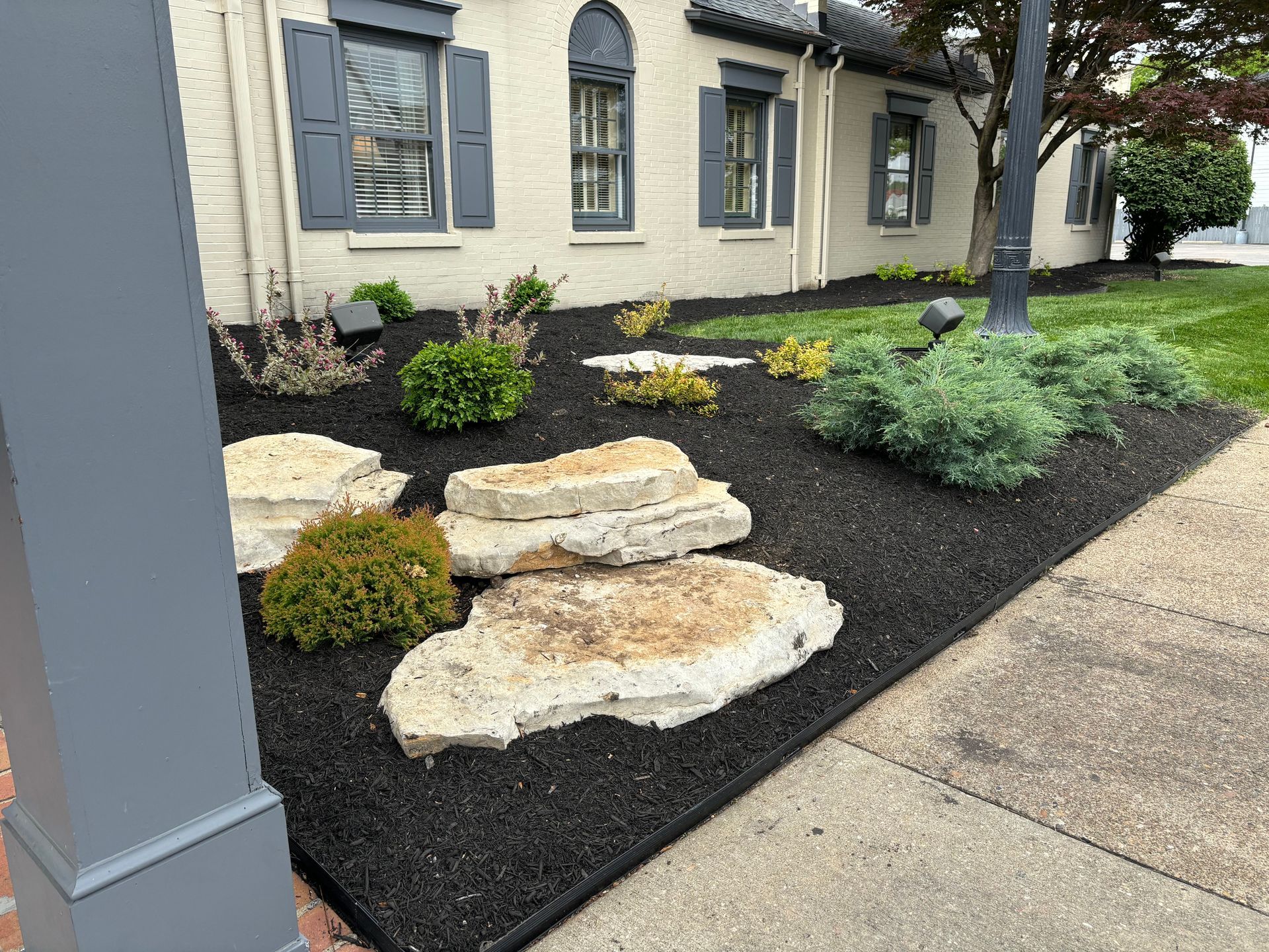 Landscaped front yard with stepping stones, shrubs, black mulch, and a beige building exterior