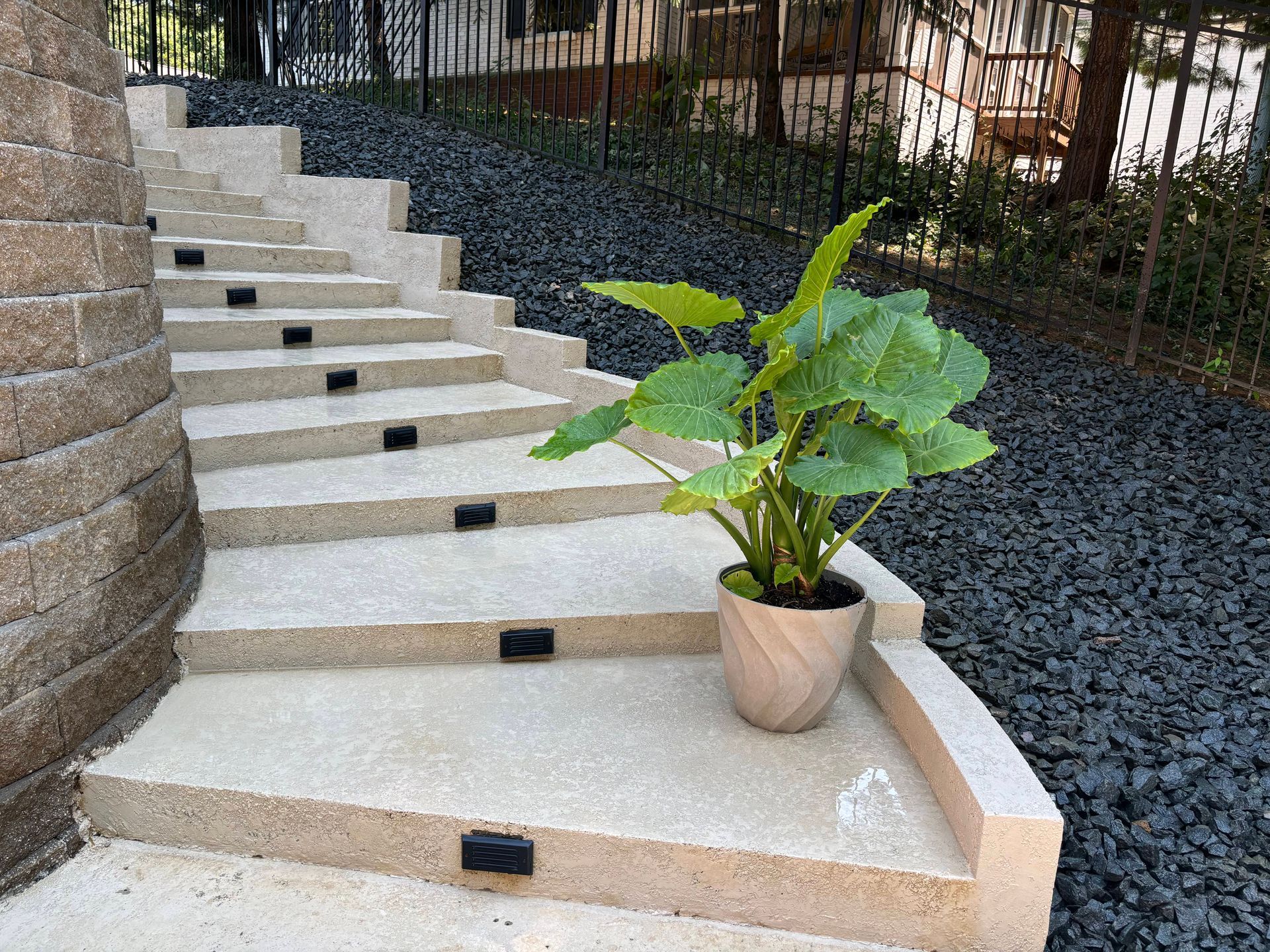 Curved outdoor steps with black lights and a potted green plant beside a stone wall.