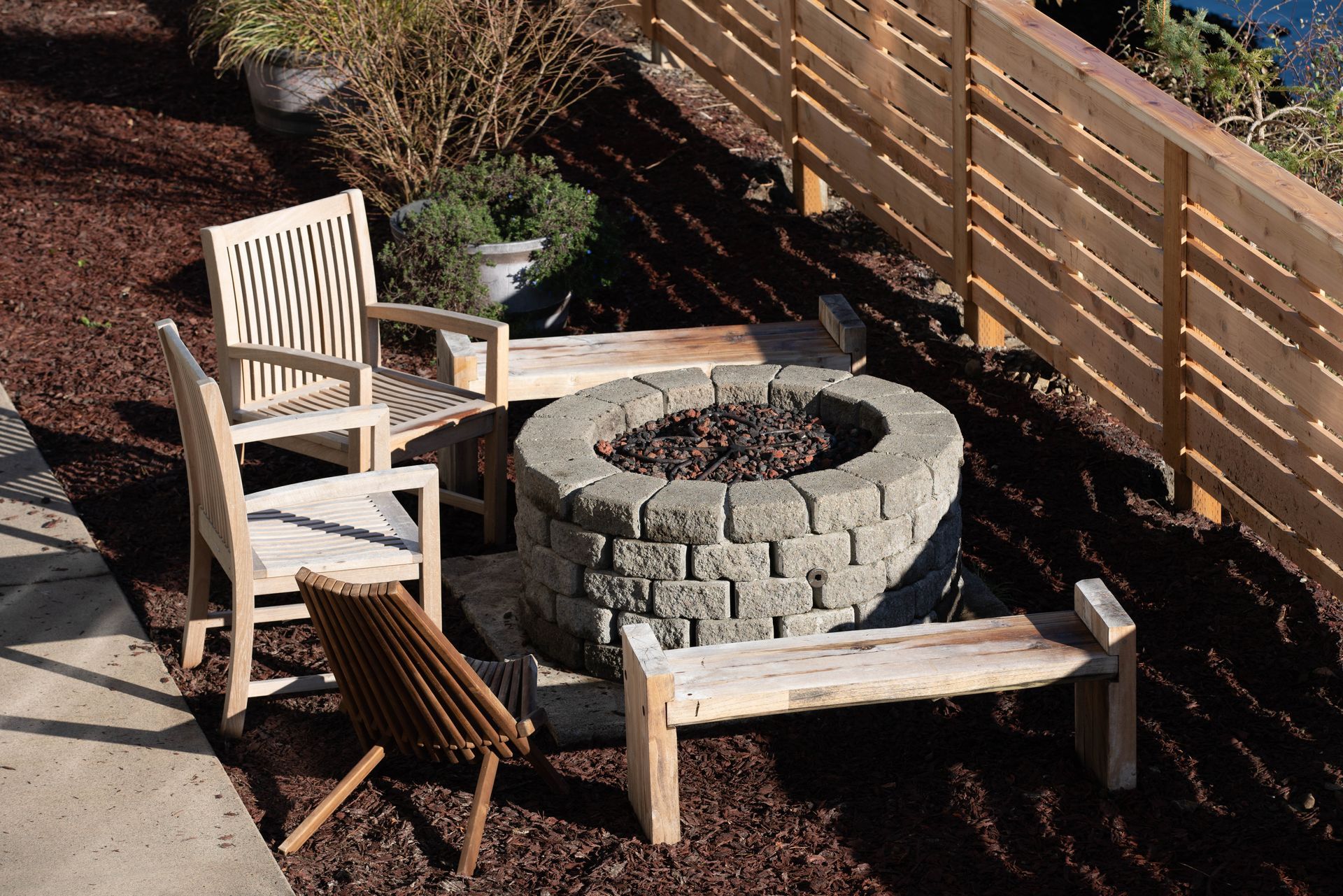 Outdoor patio with two wooden chairs, a stone fire pit, and a bench beside a wooden fence