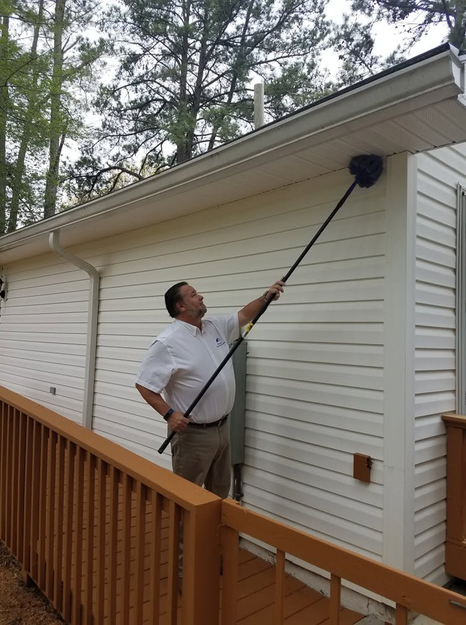 Man standing on a wooden deck beside a white house, inspecting an electrical meter and panel.