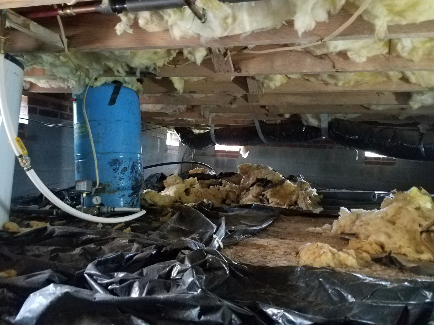 Flashlight illuminating a crawlspace with wood beams, insulation, and concrete foundation walls.