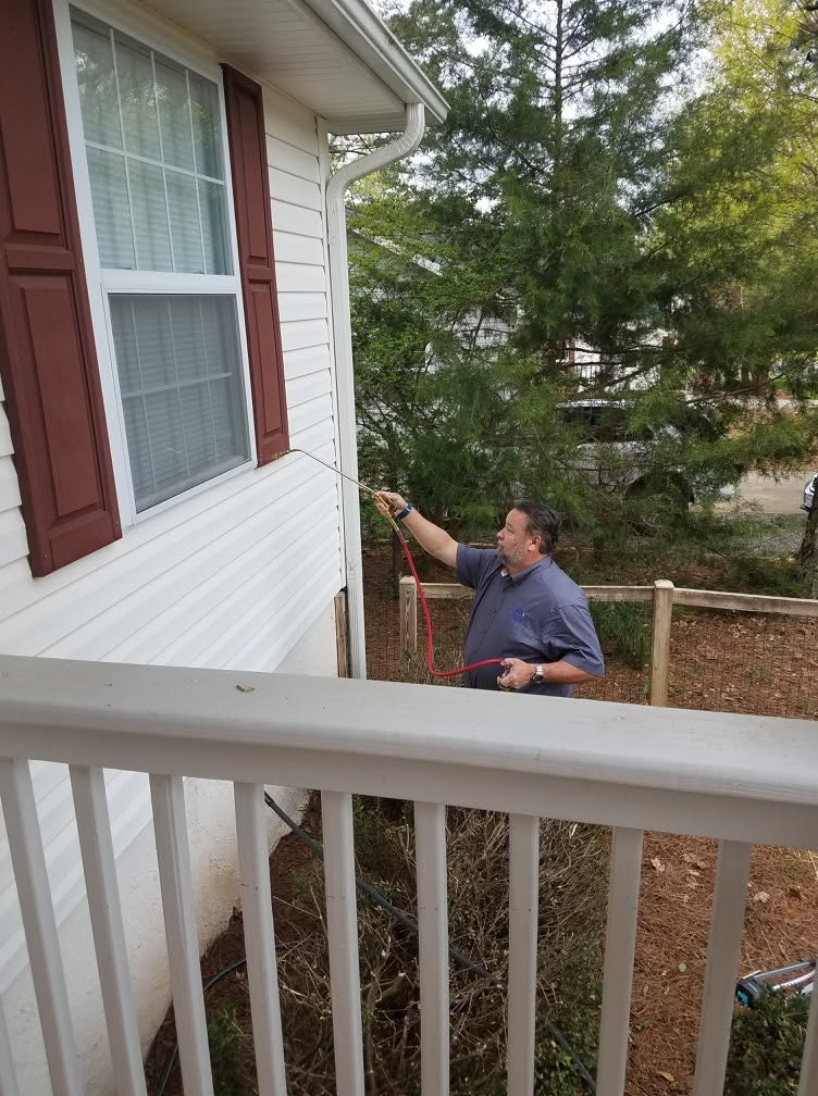 Gloved hands using a flashlight to inspect wooden baseboards near a hardwood floor