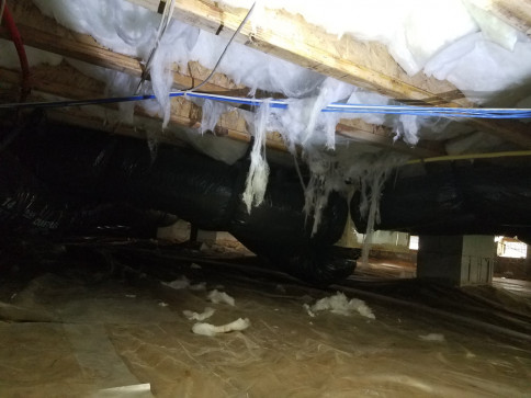 Insulated crawlspace wall with exposed wooden beams and dirt floor