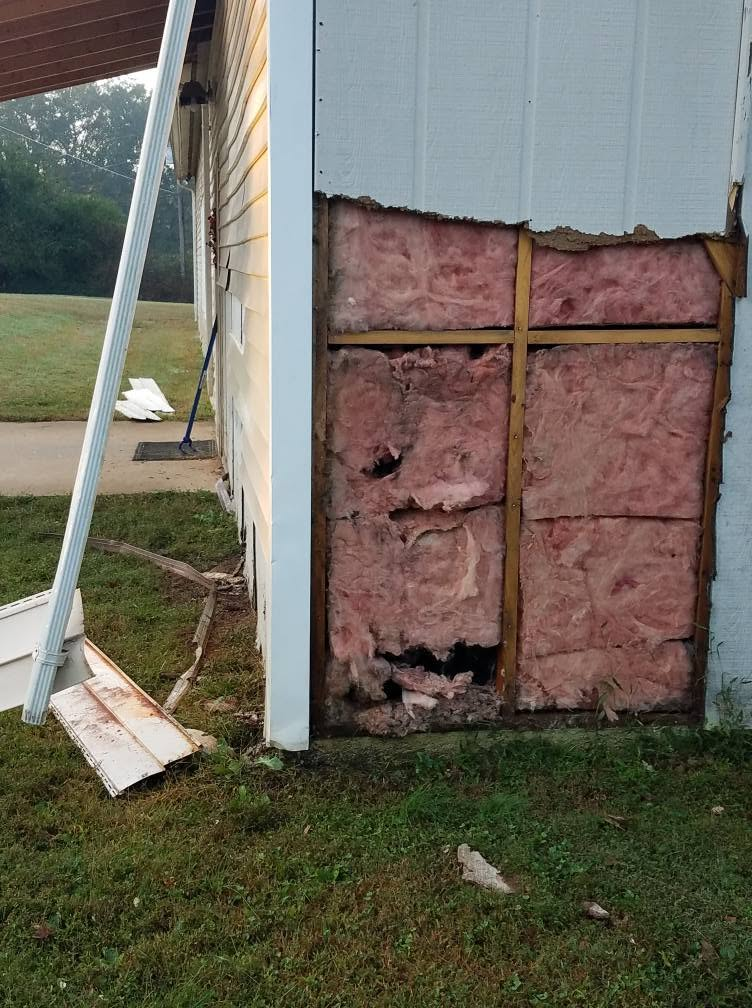 Partially insulated wall with exposed studs beside dark gray exterior siding
