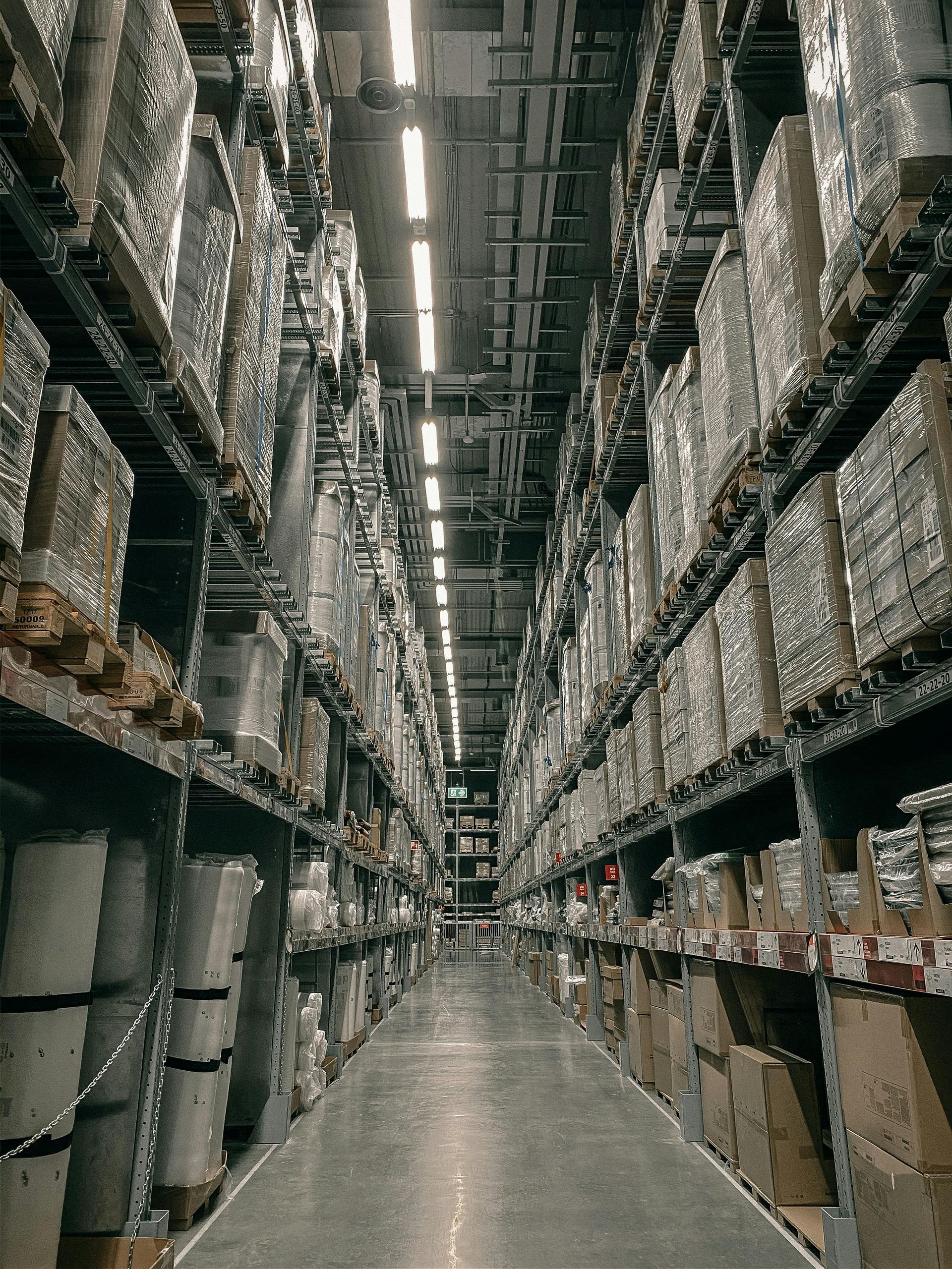 Tall warehouse aisle with high shelving, stacked boxes, and industrial supplies on both sides