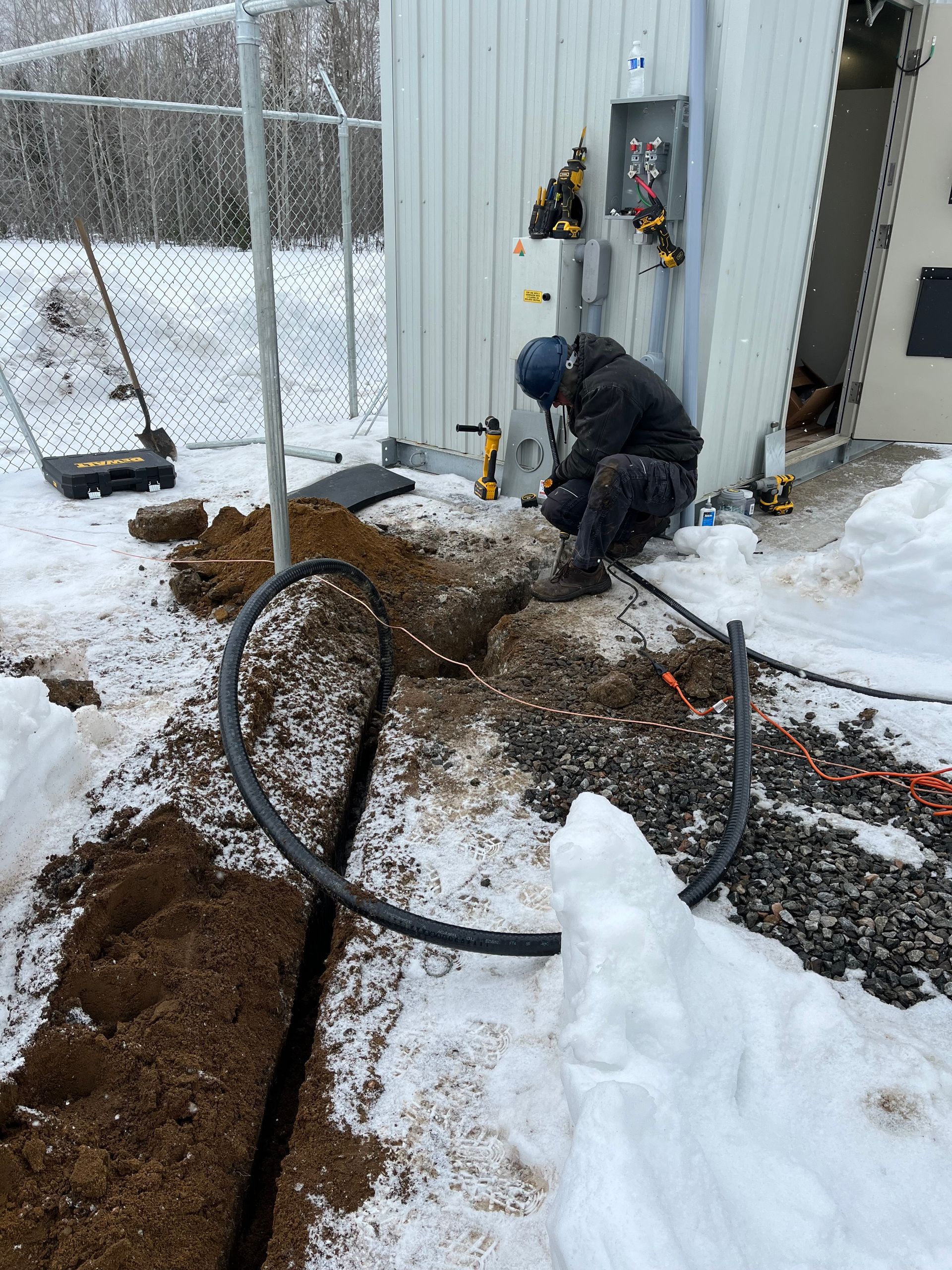 A man is working on a pipe in the snow in front of a building.