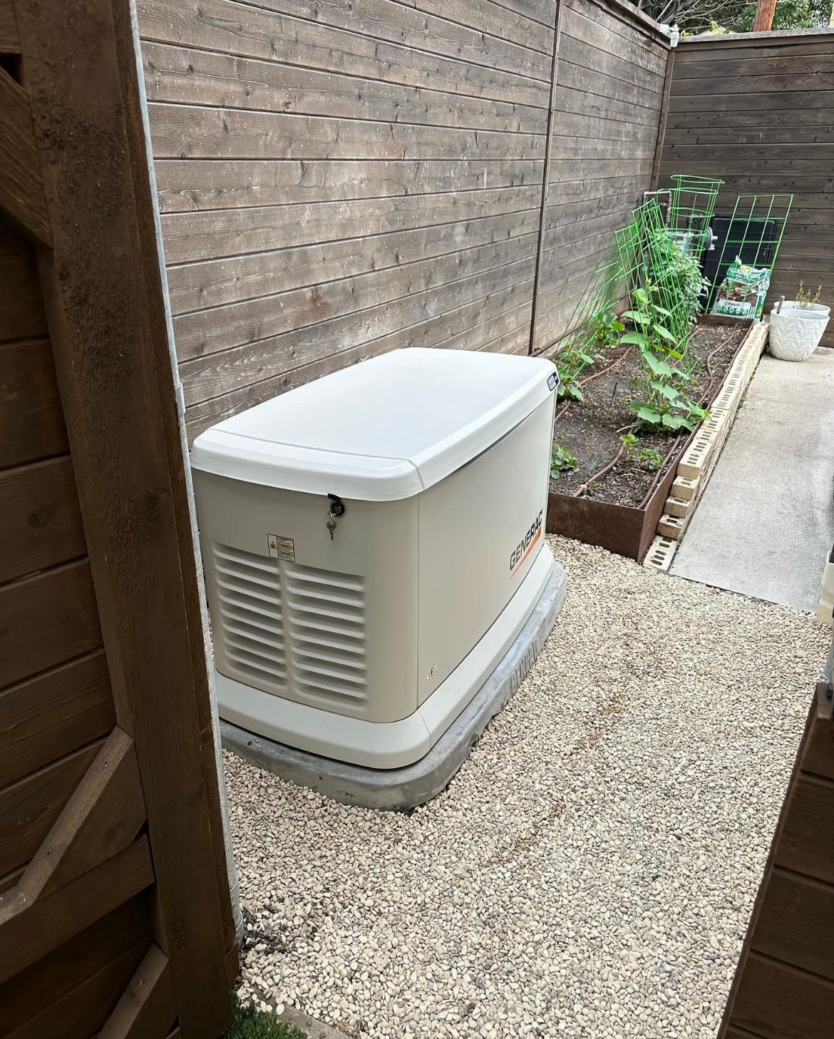 A white generator is sitting in a gravel area next to a wooden fence.