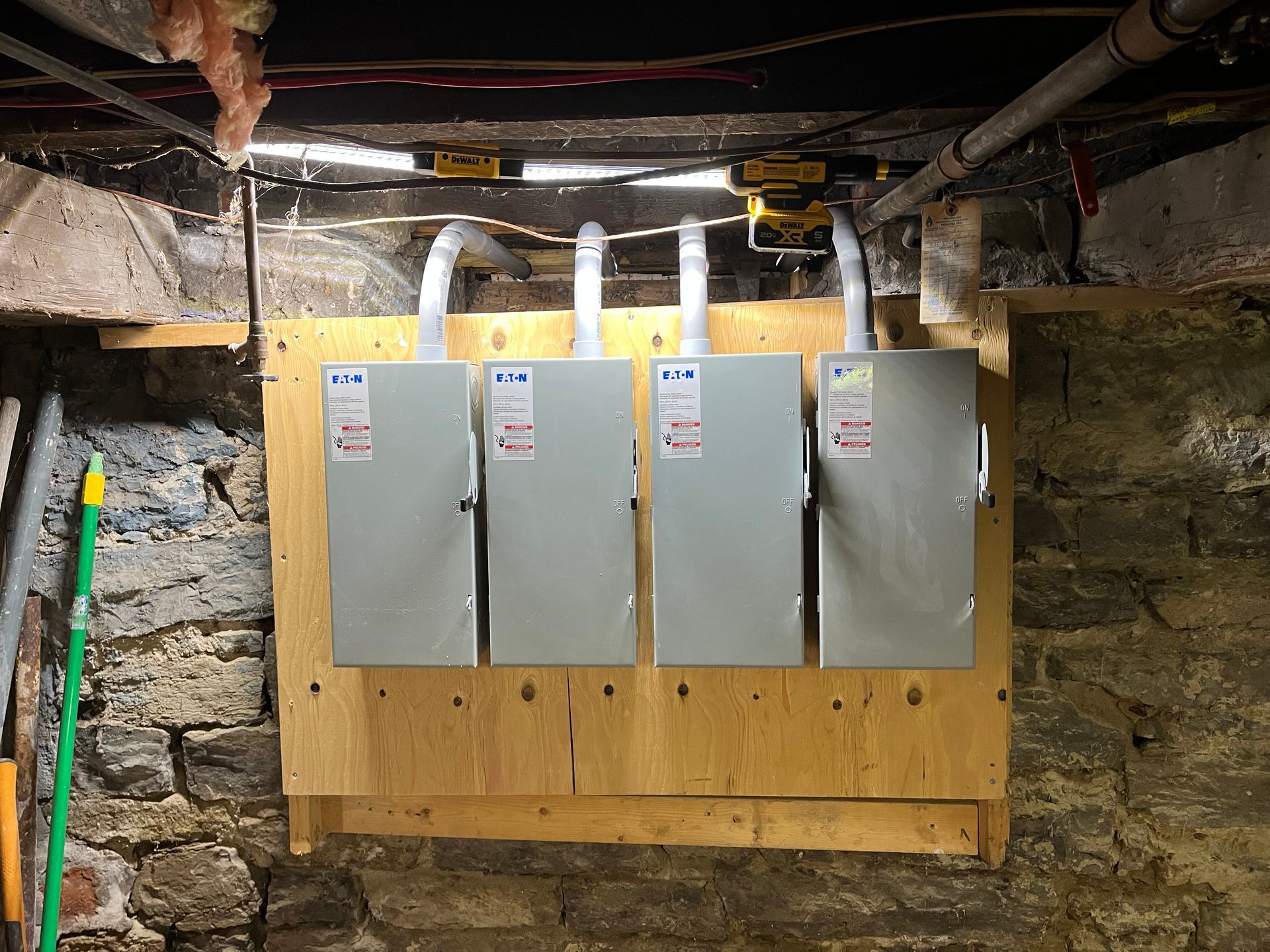 Three electrical boxes are hanging on a wooden wall in a basement.