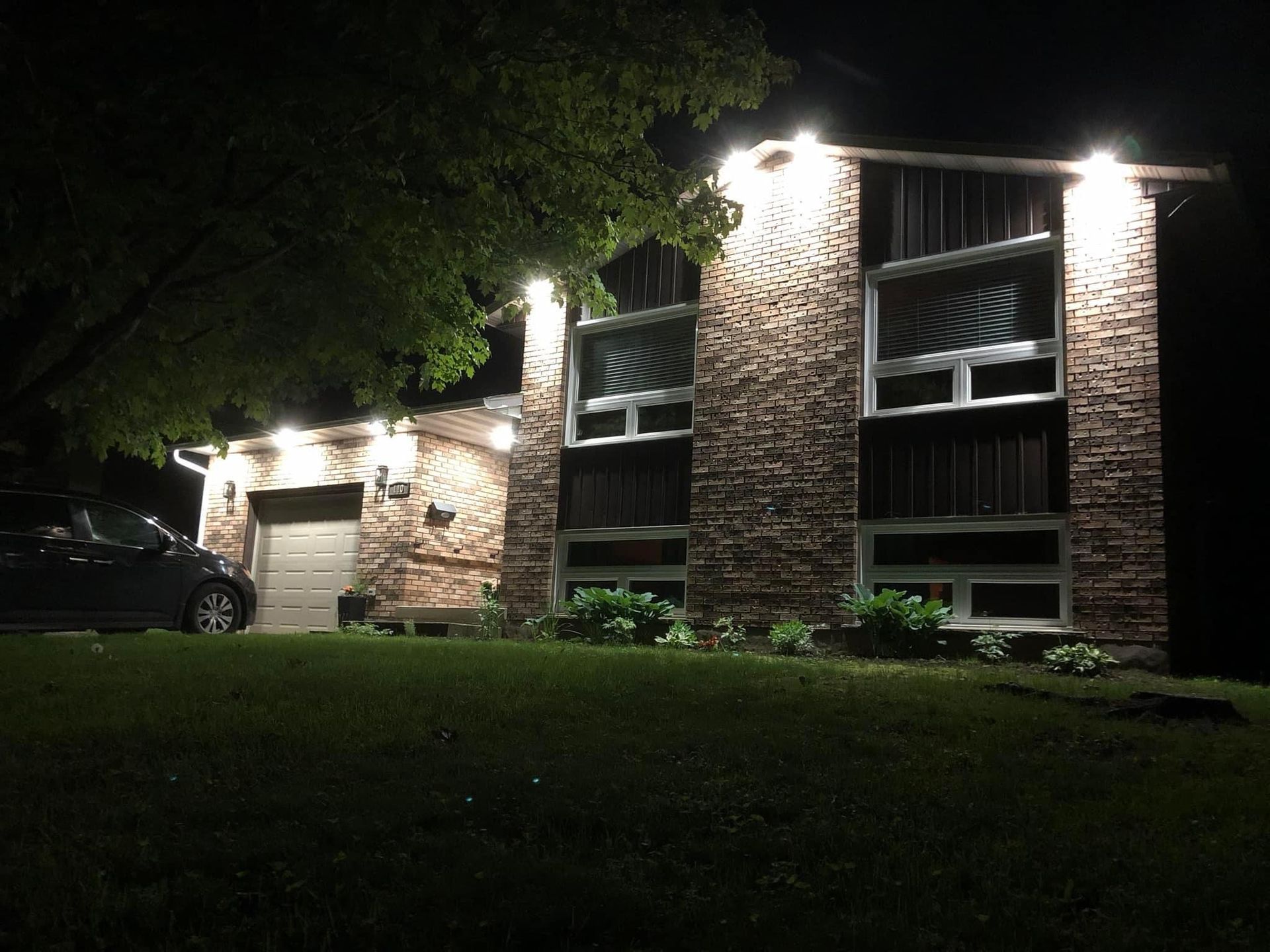 A brick house is lit up at night with a car parked in front of it.