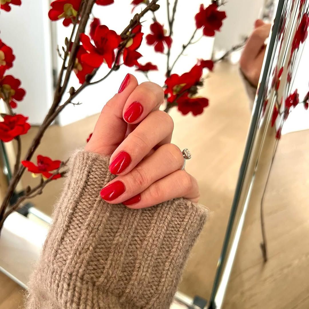Une femme aux ongles rouges tient un vase de fleurs rouges