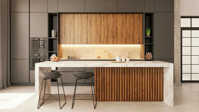 Cucina moderna e minimalista con mobili in legno, isola bianca e due sgabelli sotto una calda illuminazione sottopensile.