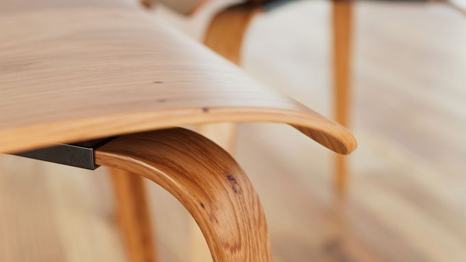 Primo piano di una sedia in legno curvato con seduta in legno chiaro e calda finitura naturale.