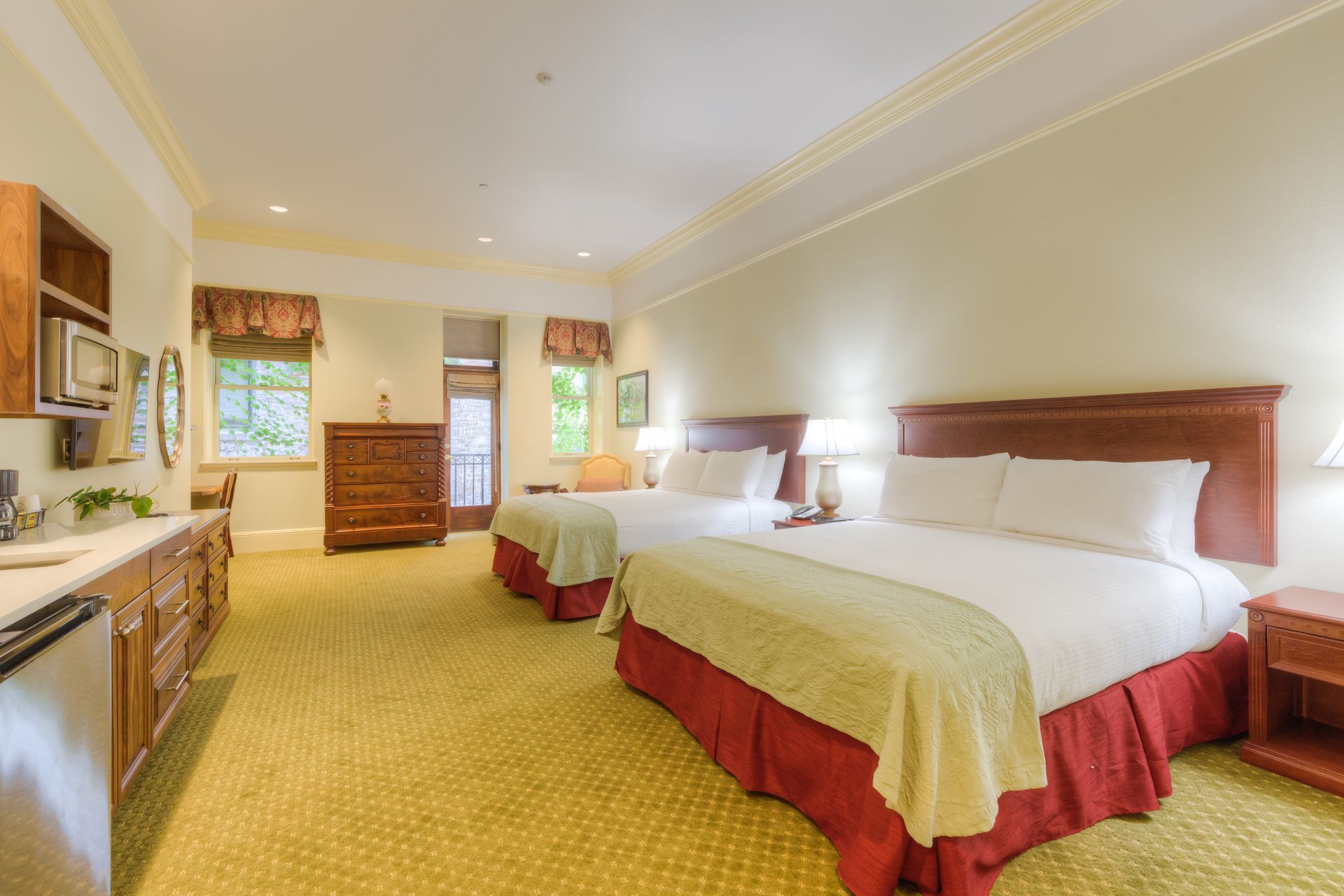 Hotel room with two queen beds, and wooden furniture. The room has a small fridge and desk area, with windows visible.