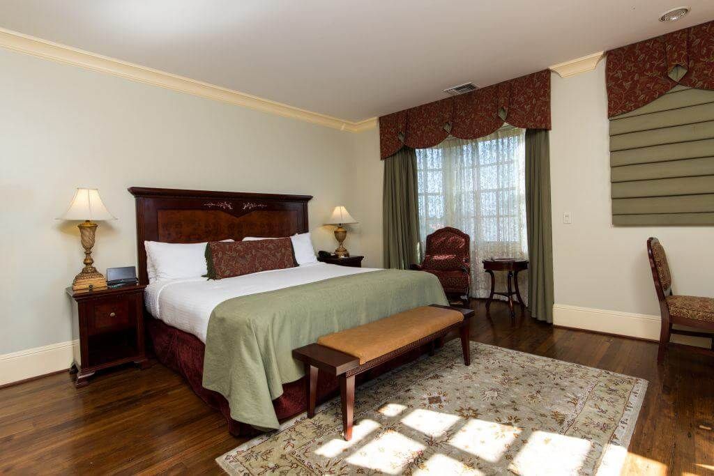 Bedroom with a dark wood bed, nightstands, and a bench. Features a green bedspread, window with curtains, and patterned rug.