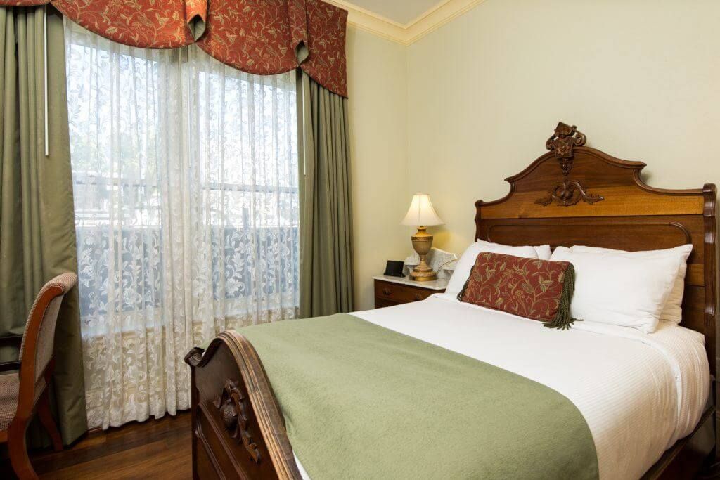 Bedroom with a wooden bed, nightstand, and window with sheer curtains and green and red drapes.