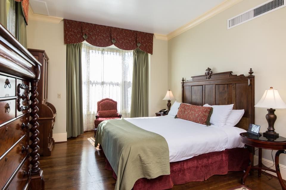 Bedroom with wooden furniture, including a bed, nightstand, and dresser. A window with curtains is behind a red chair.