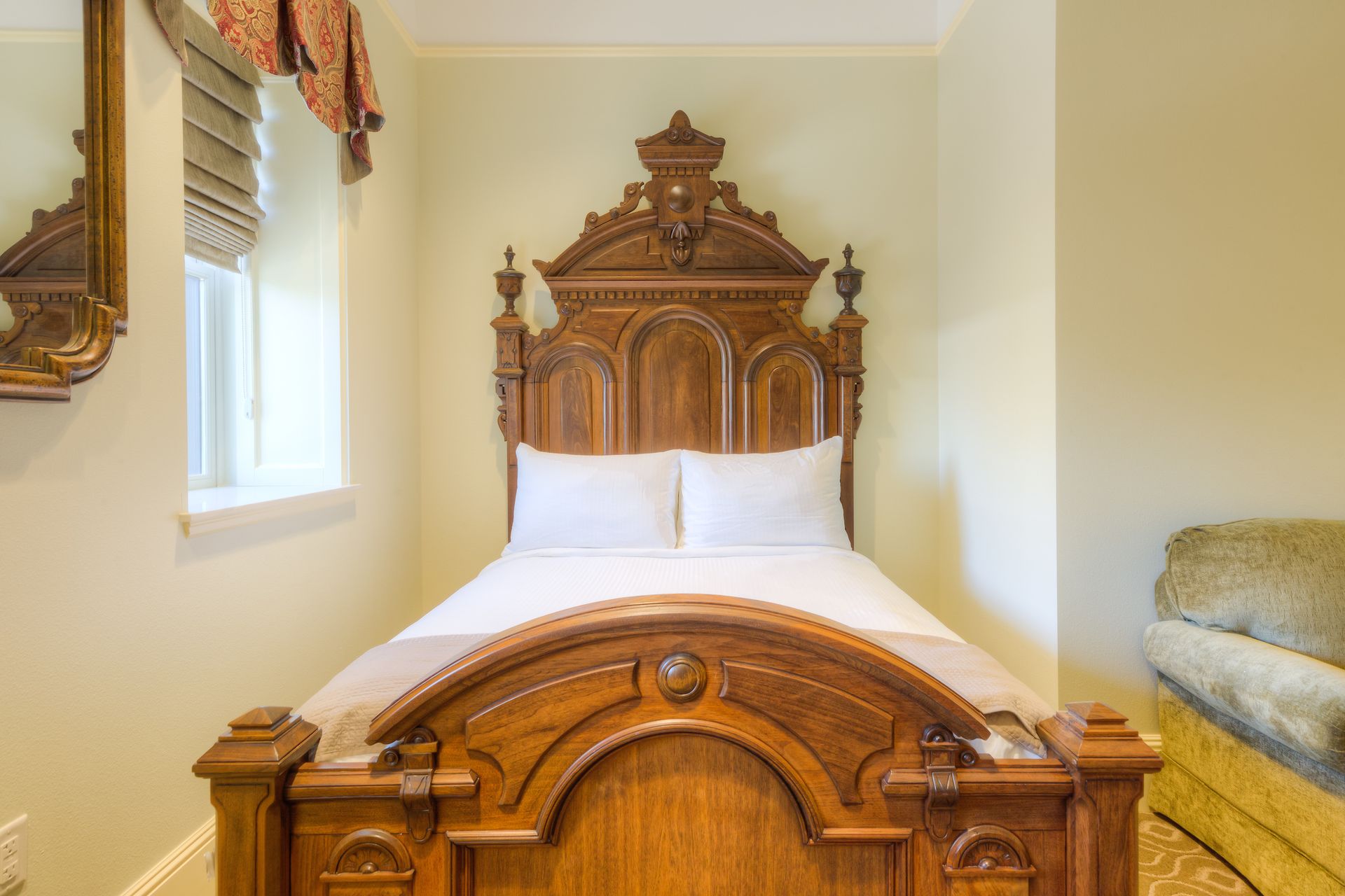 A small bedroom with a wooden antique bed and two white pillows. A small sofa is partially visible to the right.