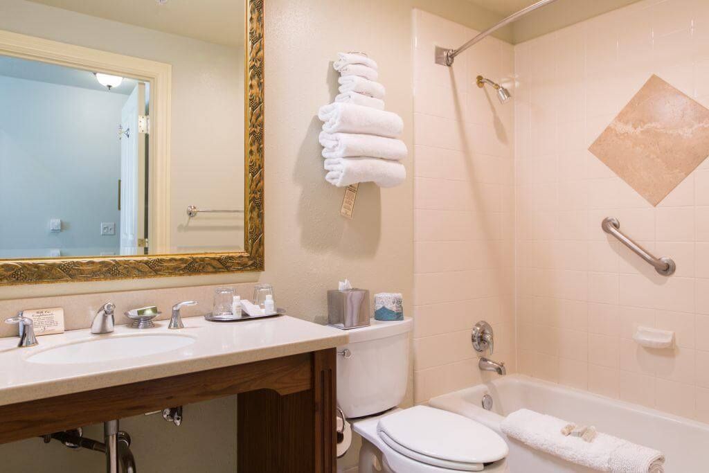 Bathroom with a white sink and toilet, beige walls, and a bathtub. A gold-framed mirror is above the sink.