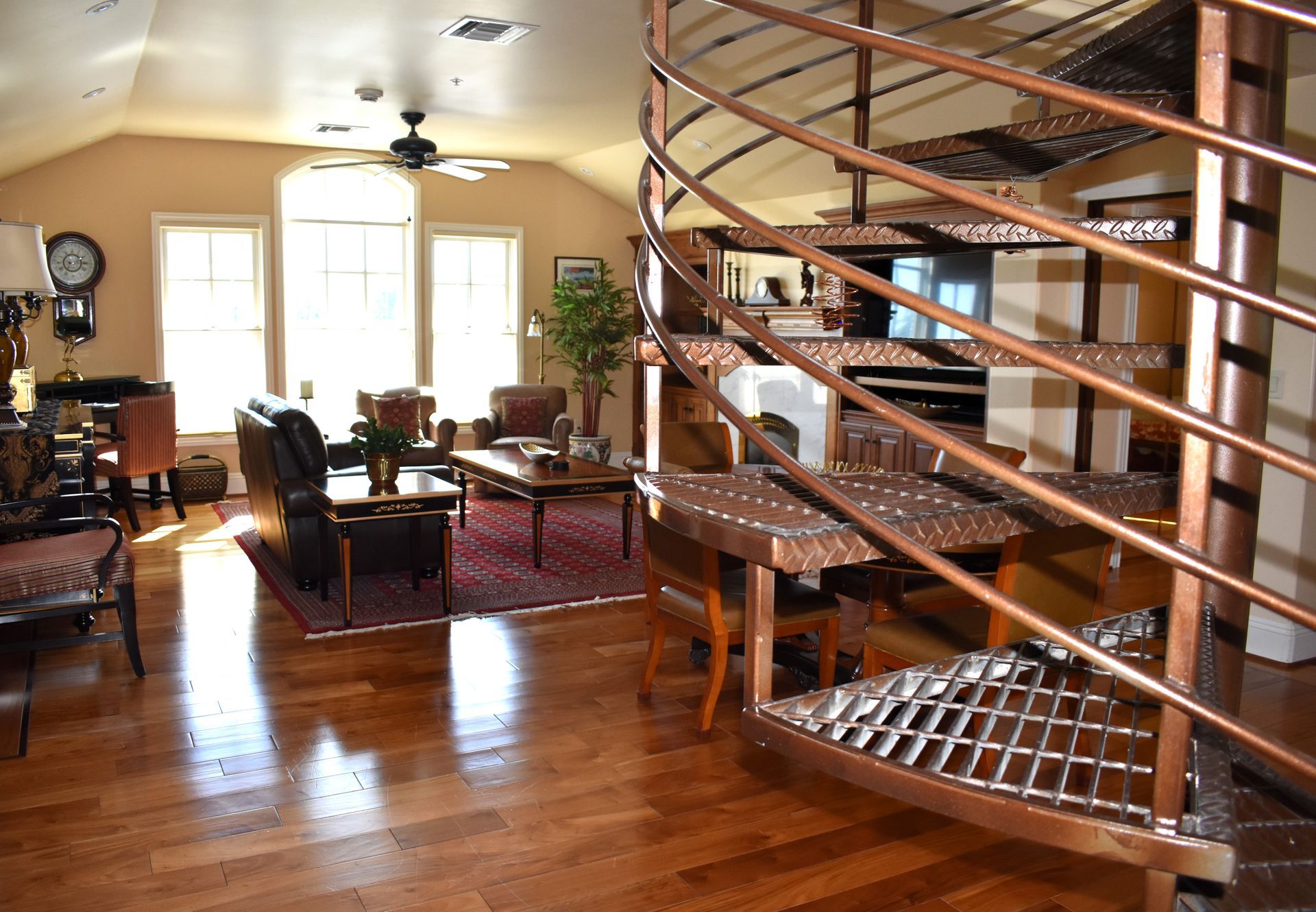 A bright interior with a copper spiral staircase, hardwood floors, and a living area with a rug, seating, and windows.