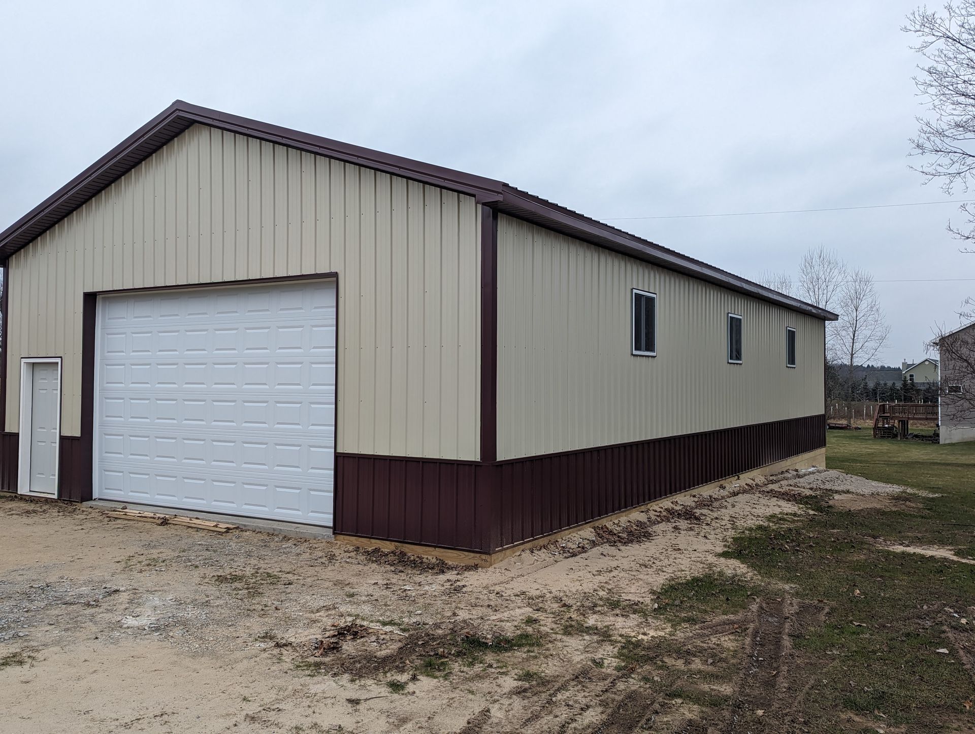 Small beige-and-brown metal garage building on a gravel lot under an overcast sky