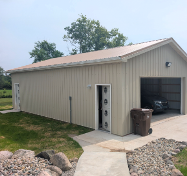 Beige metal garage with open bay, white side door, and concrete path beside a rock-lined yard.