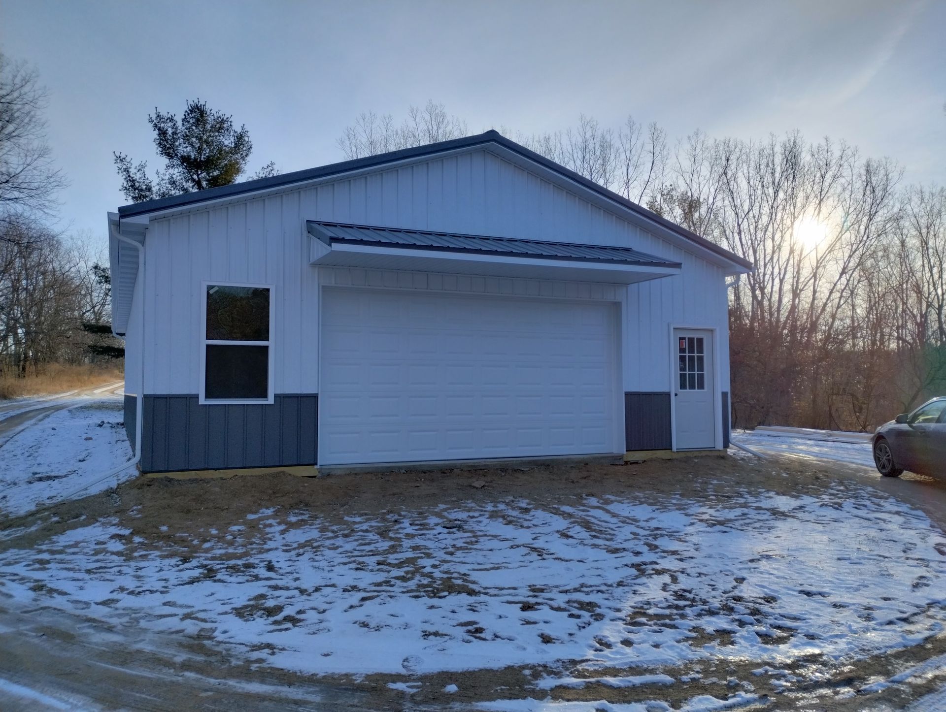 Snow-dusted white garage or shed with a roll-up door at sunset in a rural yard