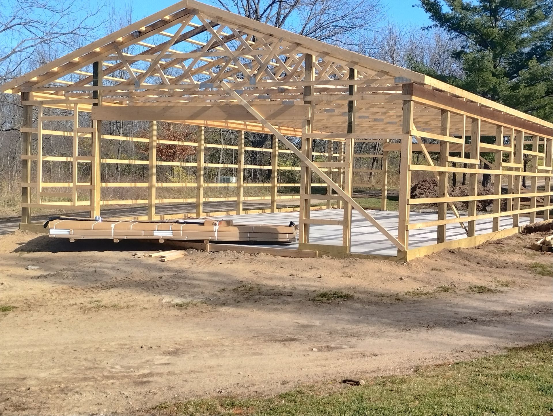 Wooden framed building under construction on a dirt lot, with trusses and open walls in daylight