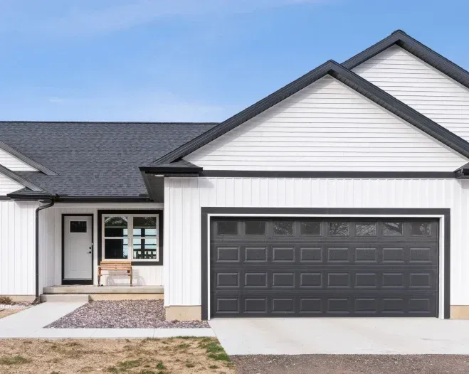 A white house with a black garage door and a gray roof.