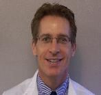 A man in a white coat and tie is smiling for the camera.