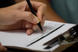 A person is writing on a clipboard with a pen.