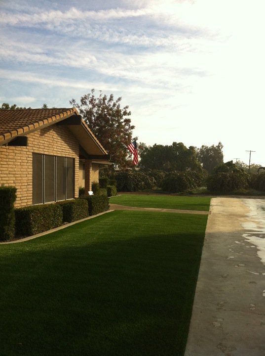 Brick house beside a green lawn and paved road under a partly cloudy sky