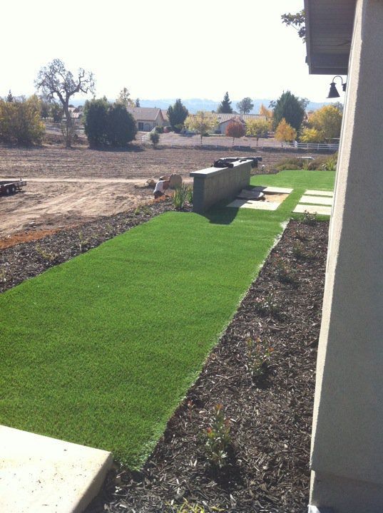 Narrow strip of bright green artificial turf beside a house in a landscaped yard.