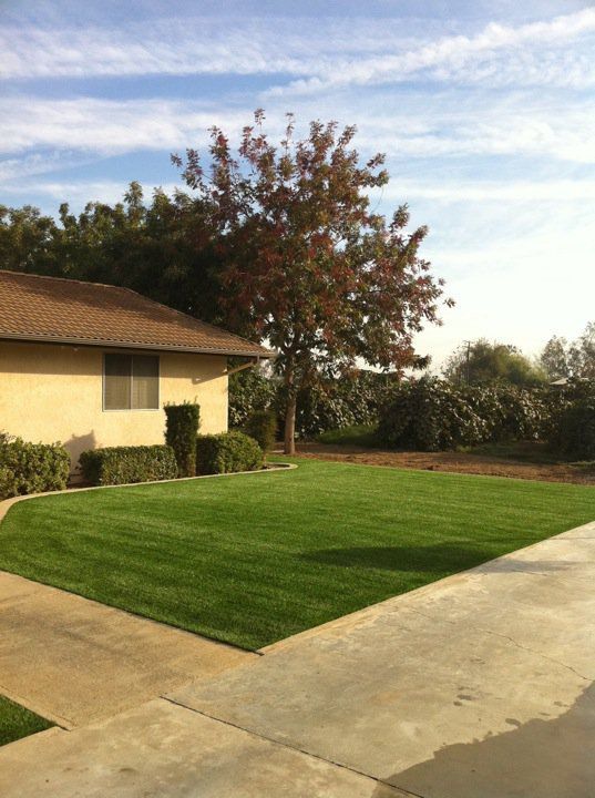 Suburban front yard with green lawn, concrete driveway, and a house under a partly cloudy sky