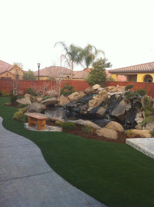 Landscaped backyard with rock garden, palm tree, and curved paved path beside a house