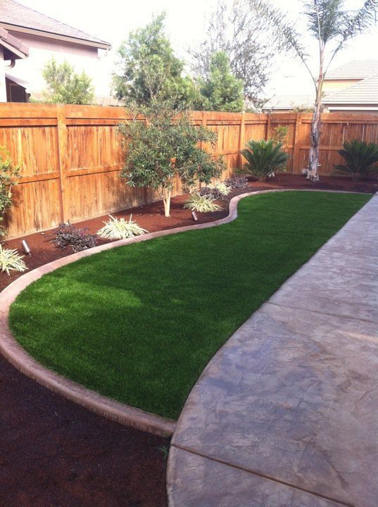 Curved backyard lawn with wooden fence, landscaped trees, and a stone patio walkway