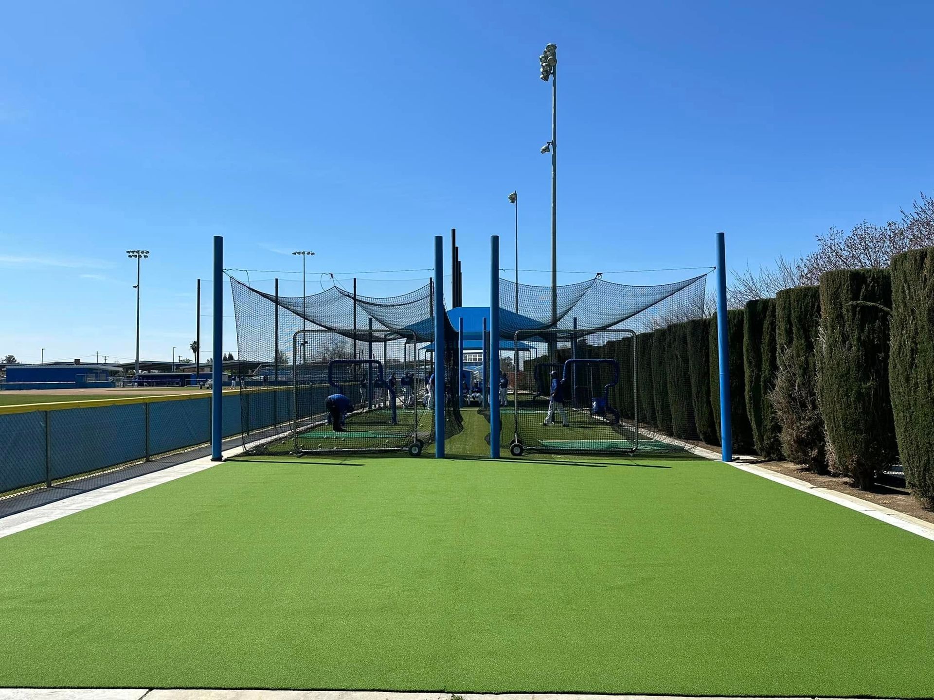 Outdoor batting cage with green turf, blue netting, and clear sky