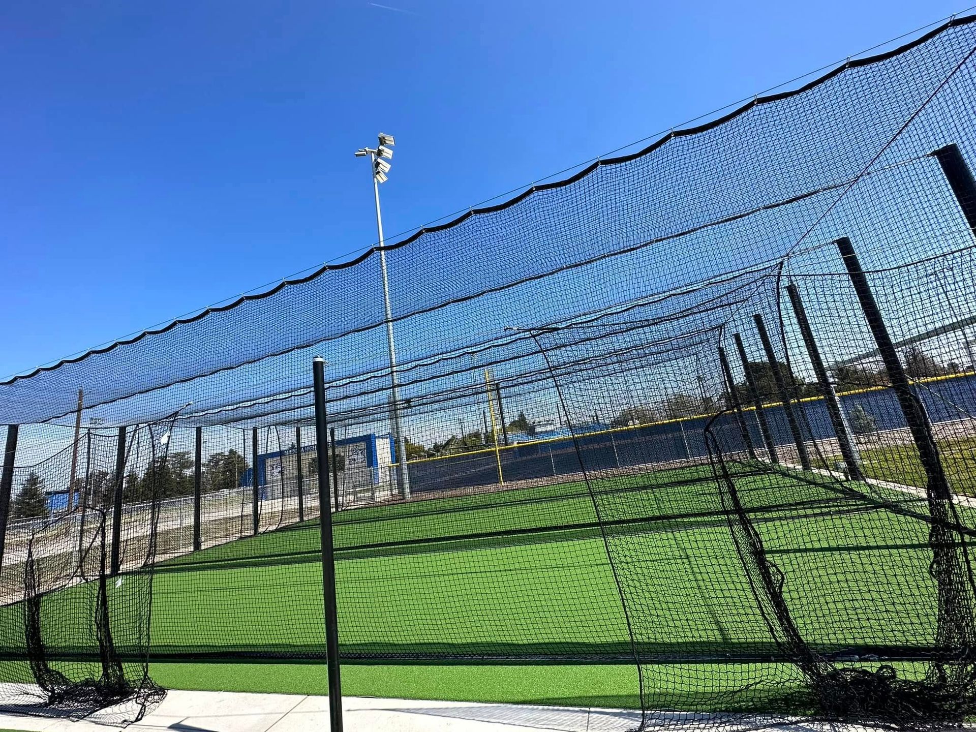 Soccer field viewed through a chain-link fence under a bright blue sky