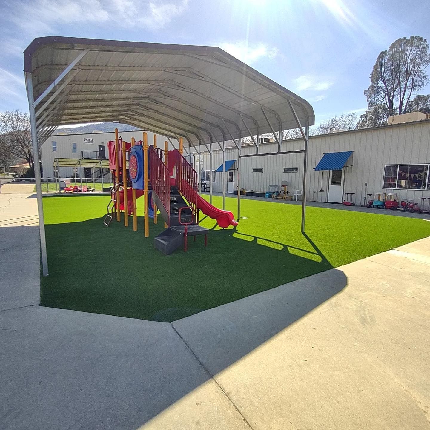 Covered playground with colorful play equipment on green turf beside a school building