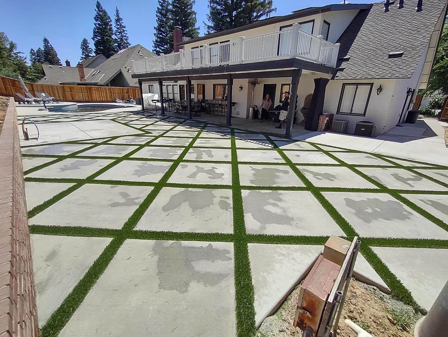 Courtyard with white stone pavers and green grass strips beside a house and patio seating