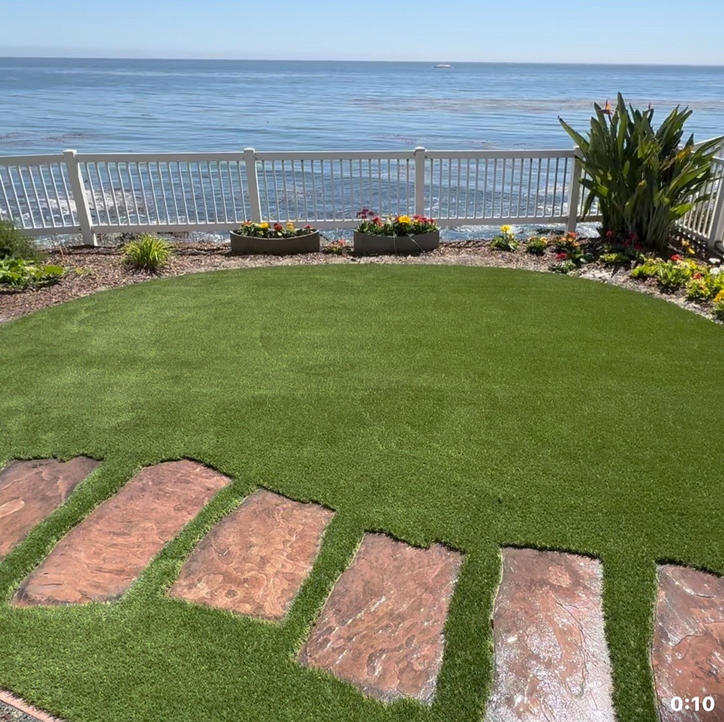 Oceanfront lawn with stone steps, white fence, and blue water beyond