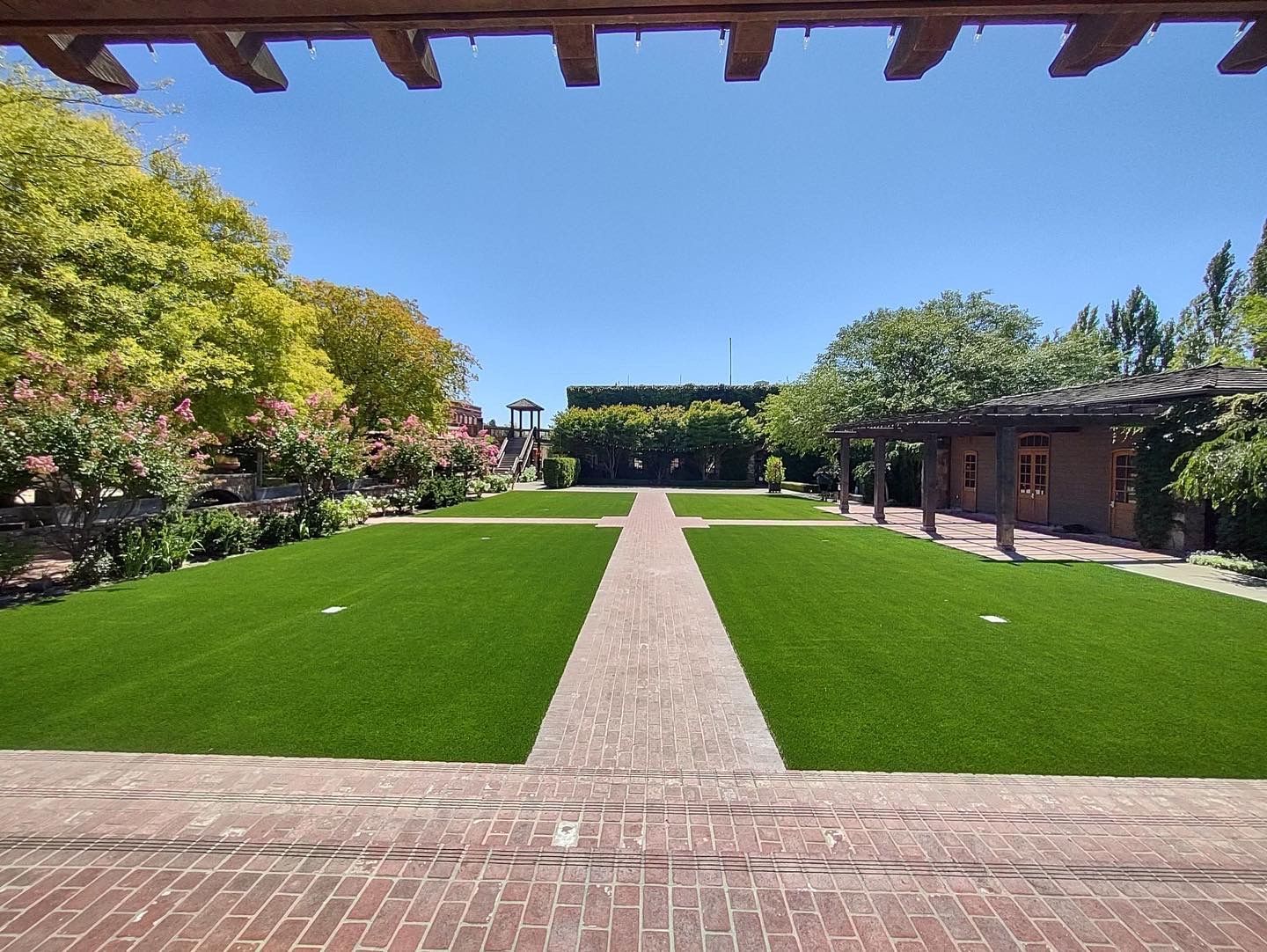 Sunny garden with a brick path leading between green lawns and trees under a blue sky