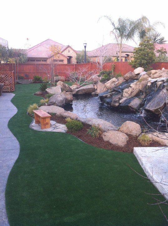 Backyard landscape with rock waterfall, pond, green lawn, and palm trees at dusk