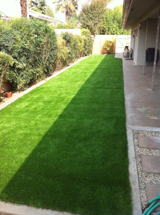 Long narrow green lawn beside a covered patio, bordered by shrubs and paved walkways