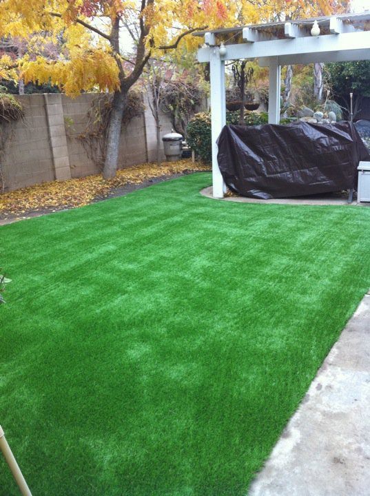Backyard with bright green artificial turf, autumn trees, and a covered patio structure.