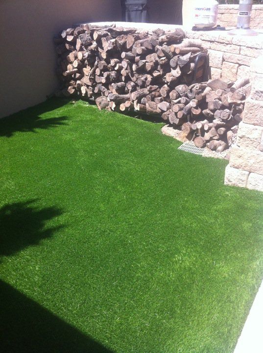 Small backyard with bright green artificial grass and a stacked stone wall in sunlight.