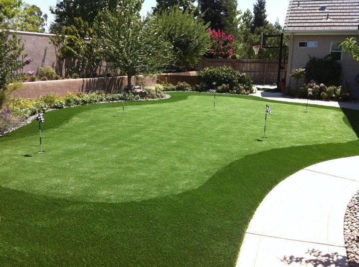 Well-manicured green backyard lawn with sprinkler heads and a curved concrete patio
